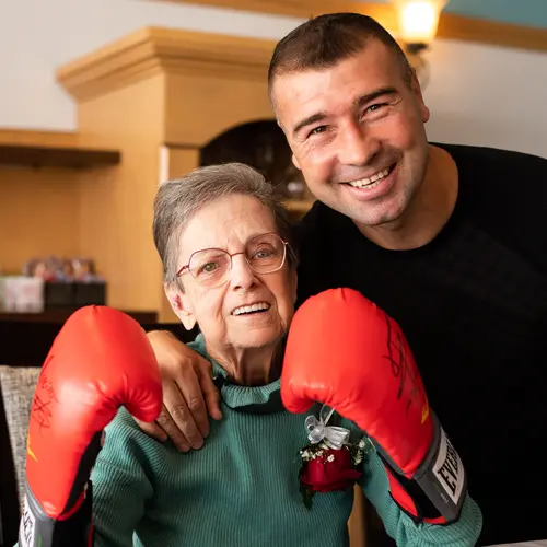 Senior woman wearing boxing gloves smiling and posing together with her favorite boxing star / Femme âgée portant des gants de boxe, souriant et posant avec sa star de boxe préférée
